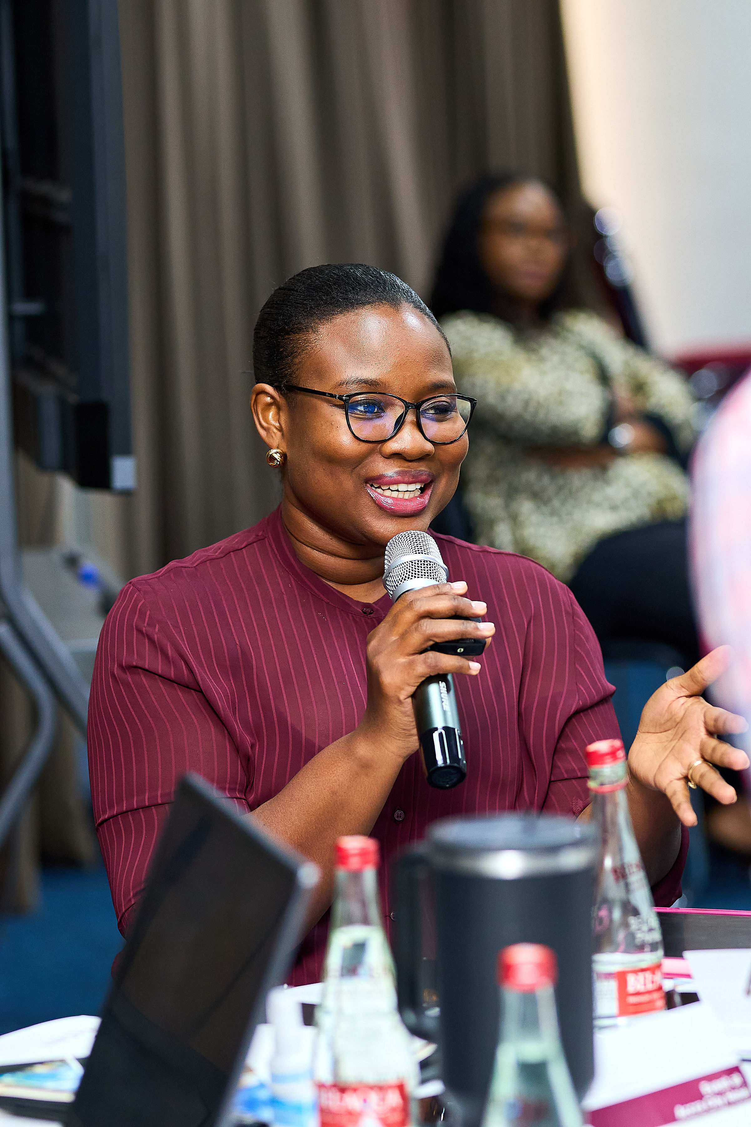 Speaker at a microphone addressing an audience, gesturing during a COME event.